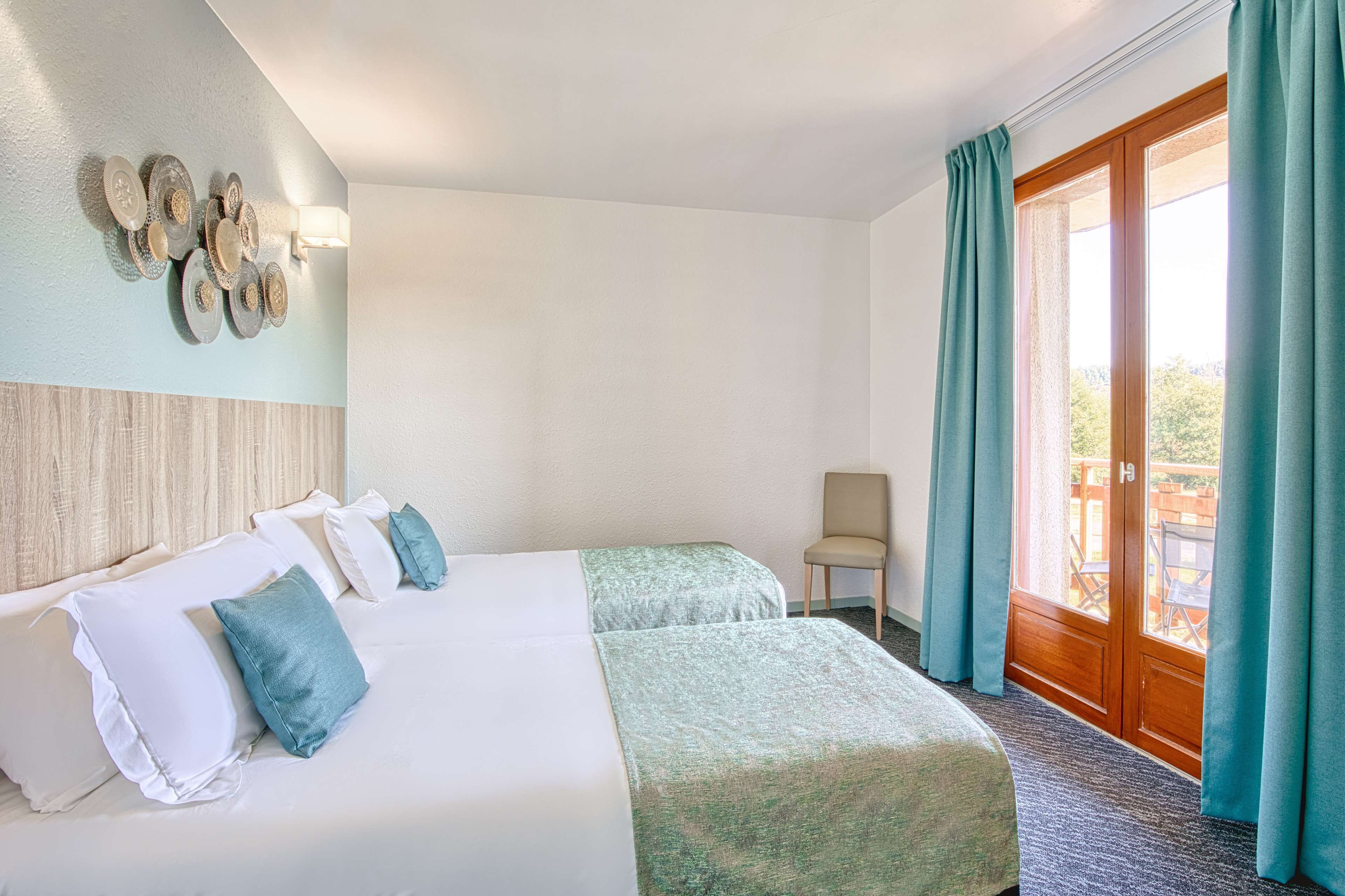 A hotel room with two beds, a wooden headboard, a wall-mounted light fixture, a chair, and a sliding glass door to the outside.