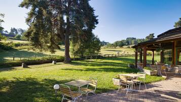 Un espace patio avec des sièges extérieurs et une vue sur un champ verdoyant et des arbres.