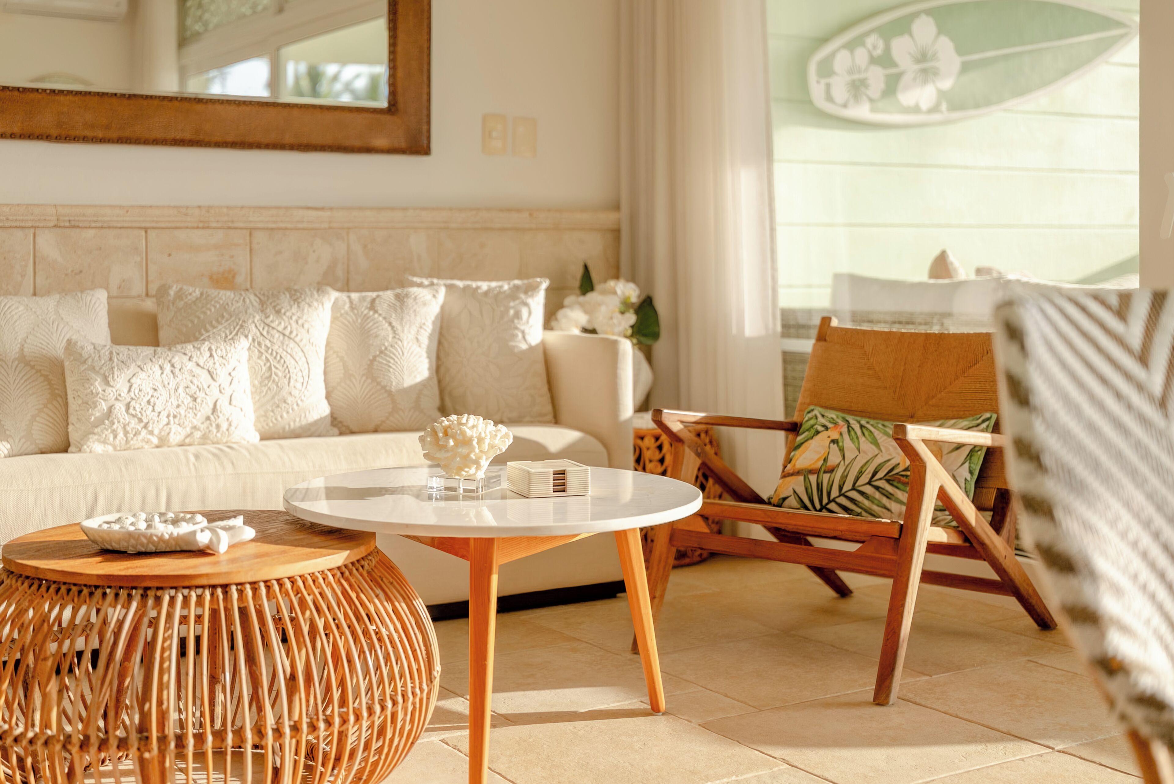 Un salon comprenant un canapé, une table basse ronde, une table d’appoint en osier et une chaise en bois avec un coussin.