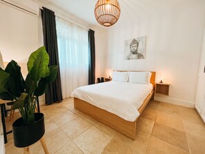 A bedroom with a large bed, a potted plant, a Buddha painting, and a hanging light fixture. - Gorgeous 2 bed 2 bath beachfront condo in Cabarete (Cabarete)