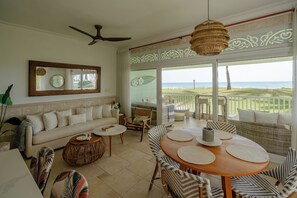 Un espacio habitable amplio con sofá, una mesa de centro y una mesa de comedor, un ventilador de techo y vistas al océano.