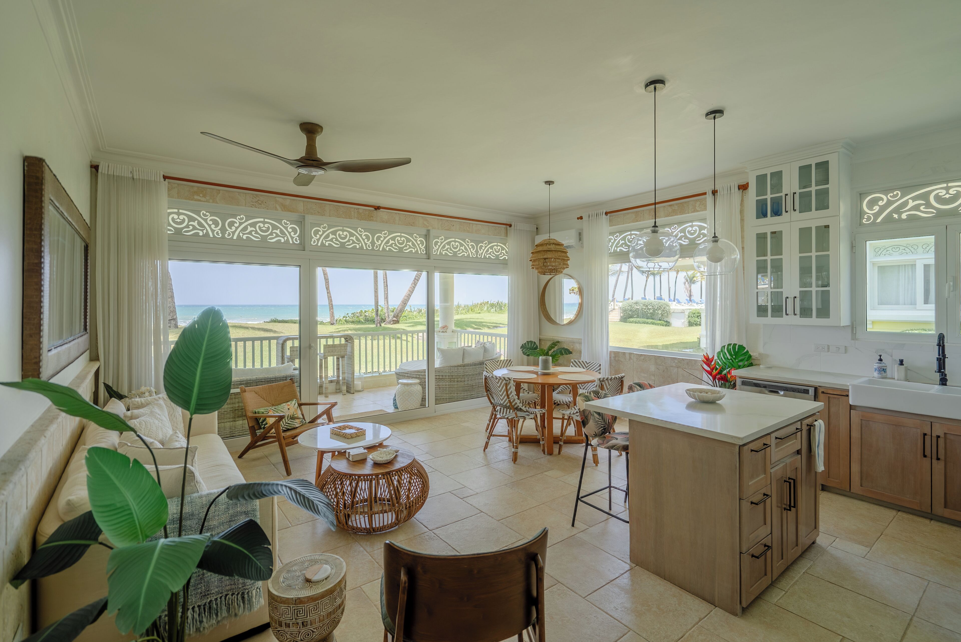 A spacious kitchen with a view of the ocean, featuring a dining area with wicker furniture and a ceiling fan.