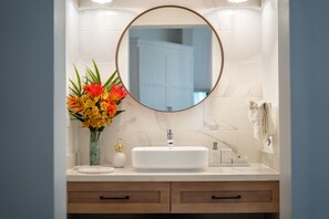 A bathroom with a white sink, a round mirror, and a vase of flowers. - Gorgeous 2 bed 2 bath beachfront condo in Cabarete (Cabarete)