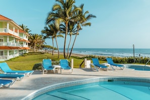 A pool area with lounge chairs and a view of the ocean.