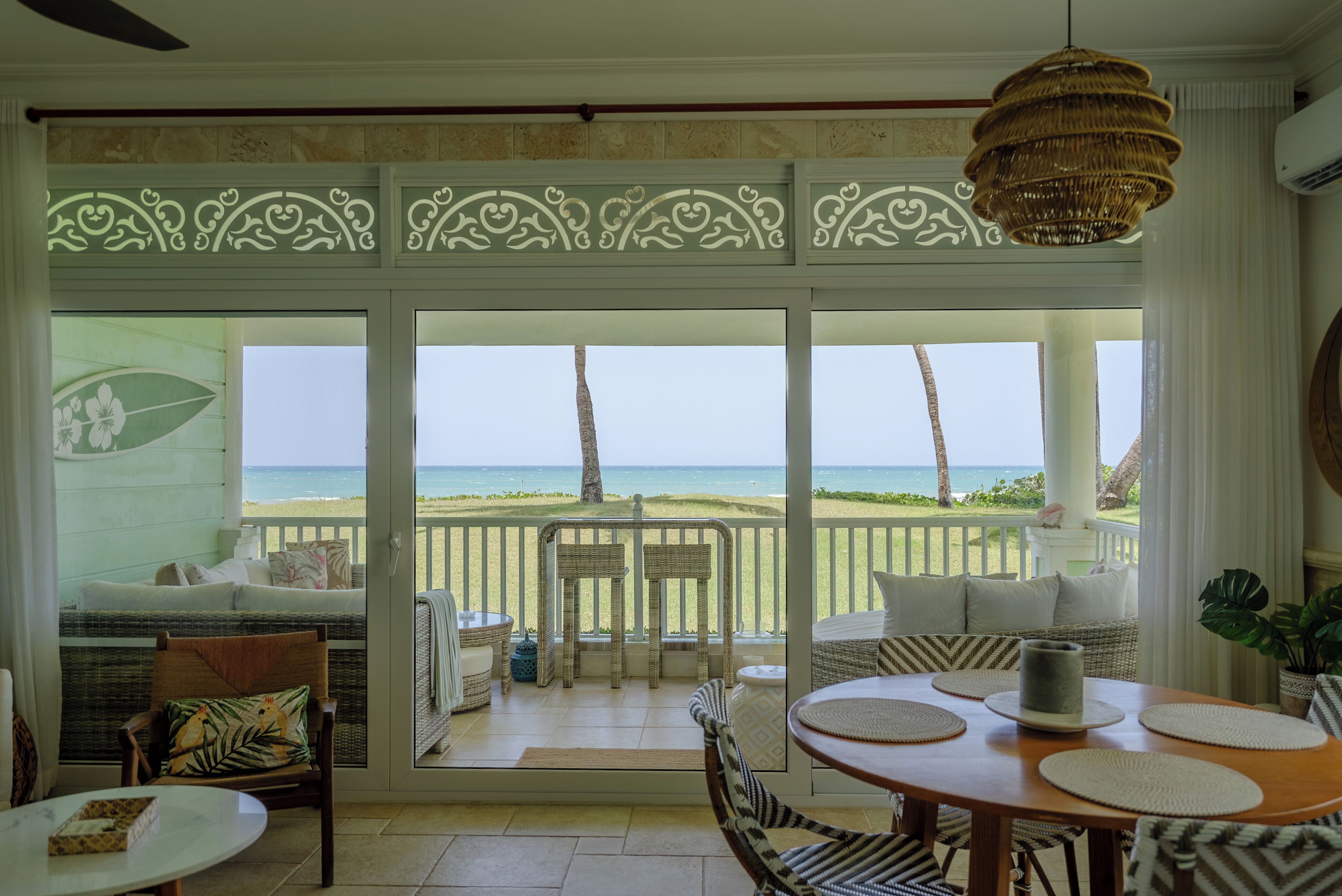 Une chambre avec vue sur la plage, un coin repas avec une table et des chaises, et un balcon avec un fauteuil en osier.