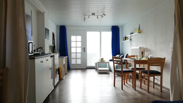 A modern kitchen with white cabinets, a dining area with wooden chairs, and a large window with blue curtains. - Frisch Renoviertes, Lichtdurchflutetes Apartment! (Runkel)