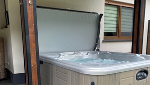 Ein Whirlpool mit Holzrahmen und Bedienfeld, gelegen in einem Außenbereich mit Fliesenboden und einem Fenster mit Jalousien.