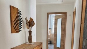 A hallway with a wooden cabinet, a vase with dried plants, and a door leading to another room.