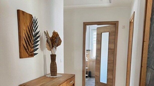 Ein Flur mit einem Holzschrank, einer Vase mit Trockenpflanzen und einer Tür zu einem anderen Raum.