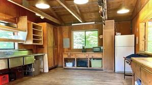 A rustic kitchen with wooden cabinets, a stainless steel sink, and a refrigerator.