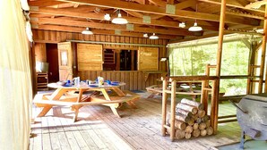 A rustic wooden cabin with a dining table set for four, a grill, and a stack of firewood.