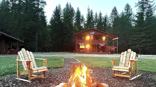 A cabin with a fire pit in the center, surrounded by two Adirondack chairs.