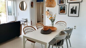 A dining area with a white table, wicker chairs, and a hanging light fixture.