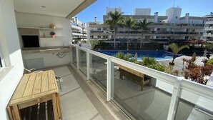 Ein Balkon mit Holztisch und Bank, mit Blick auf einen Swimmingpool und Wohnhäuser.