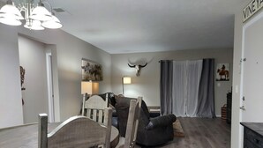 A living room with a dining table, chairs, a sofa, a lamp, a wall-mounted deer head, and a painting. - Mystic Ranch Condo (Branson)