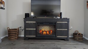 A modern fireplace with a flat-screen TV above it, two woven baskets on either side, and a brick wall in the background. - Mystic Ranch Condo (Branson)