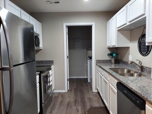 Una cocina moderna con electrodomésticos de acero inoxidable, encimeras de granito y armarios blancos.