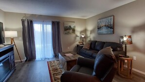 A living room with a sofa, armchair, TV, lamp, and artwork on the wall.