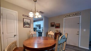 A dining room with a wooden table and chairs, a kitchen in the background, and a sign that reads "VINEYARD".