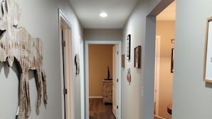 A hallway with wooden flooring, white walls, and a door leading to another room.
