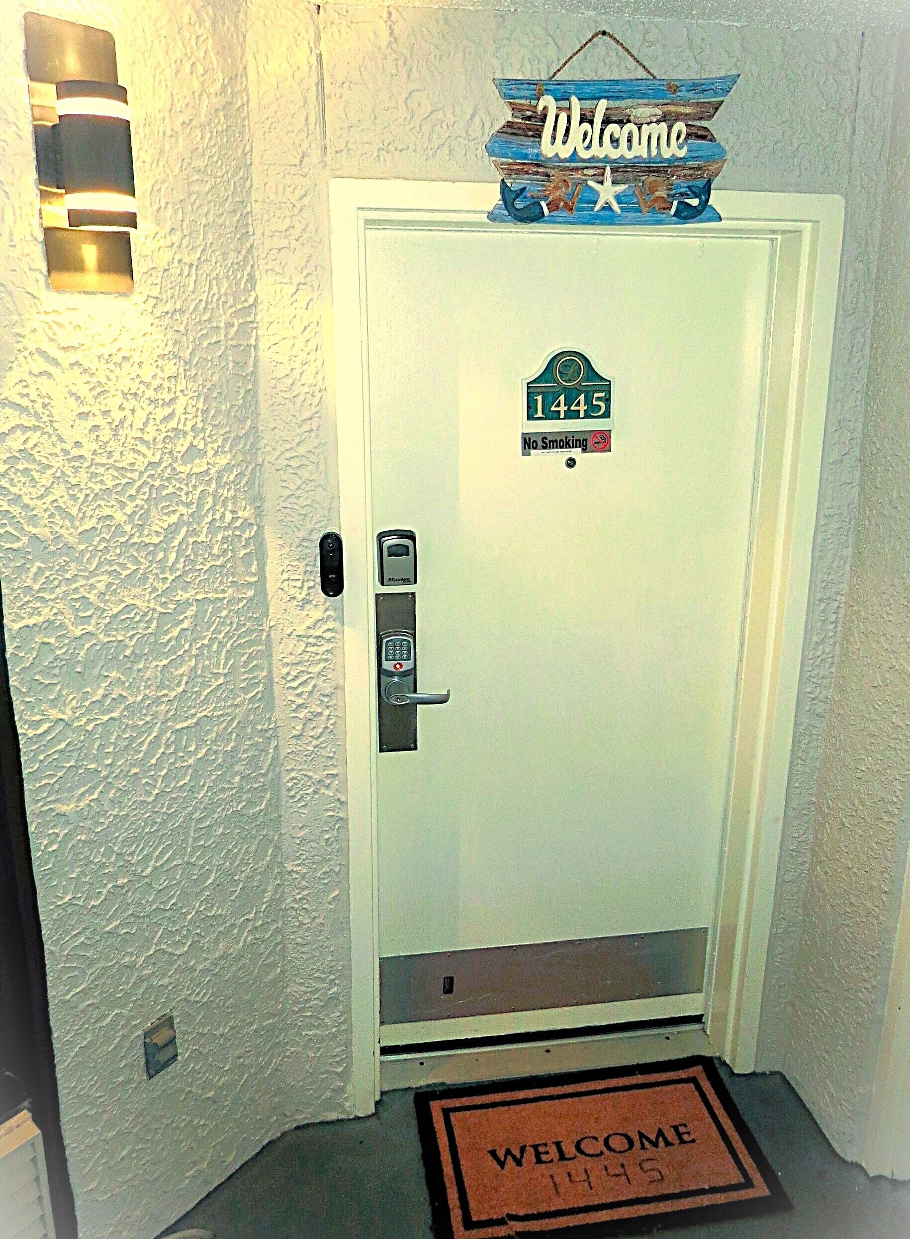 A white door with a 'Welcome' sign, a 'No Smoking' sign, and a keypad lock.