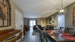 A spacious living area with a dining table set for four, a sofa, and a fireplace. - Serenity Now (Branson)