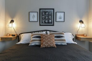 A neatly made bed with patterned pillows, a framed botanical print above it, and two wall-mounted lamps on either side. - Serenity Now (Branson)