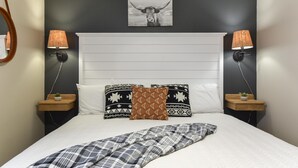 A bedroom with a white headboard, two bedside tables with lamps, patterned pillows, and a blanket. - Serenity Now (Branson)