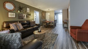 A living room with a leather sofa, a coffee table, and a dining area with a wooden table and chairs. - Serenity Now (Branson)