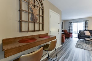 A modern living room with a wooden dining table, two chairs, a red rug, a sofa, and a large window with curtains. - Serenity Now (Branson)