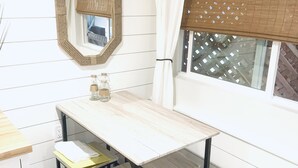 Ein kleiner, ordentlicher Raum mit einem Holztisch, zwei Stühlen, einem Spiegel und einem Fenster mit Vorhang.