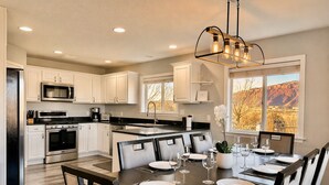 A modern kitchen with white cabinets, stainless steel appliances, and a dining area with a dark wood table set for six.