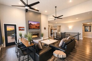 Una sala de estar moderna con chimenea, muebles de cuero, ventiladores de techo y vistas al exterior.