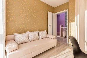 A beige sofa with floral cushions, a black chair, and a patterned wall.