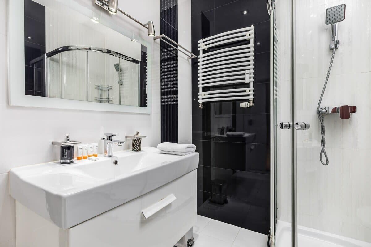 A modern bathroom with a large mirror, a white sink, a glass shower enclosure, and a towel rack.