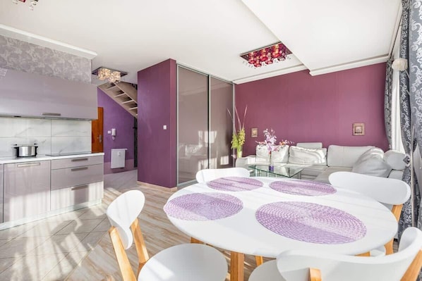 A modern kitchen with a white countertop, a dining area with a white table and chairs, and a purple wall.