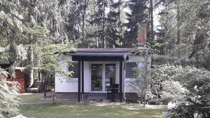Een modern huis met een overdekte veranda, omgeven door dichte bomen en een verzorgd gazon.