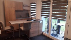 Een kleine keuken met een barstoel, een inbouwspoelbak en een raam met zonwering.