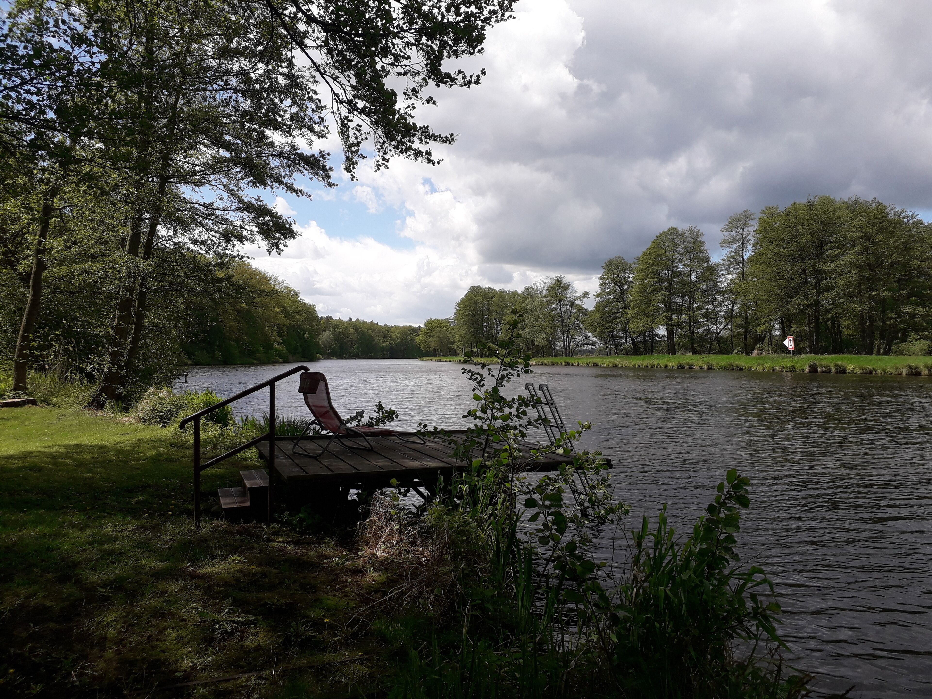 A wooden dock extending into a calm lake surrounded by lush greenery and trees.