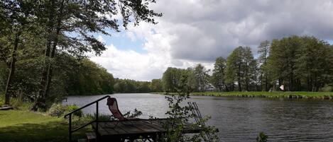 A wooden dock extending into a calm lake surrounded by lush greenery and trees.