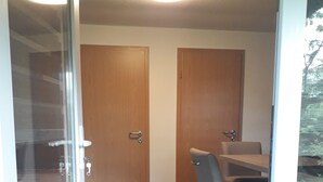 Een vergaderruimte met een glazen wand, twee houten deuren, een tafel met stoelen en een vloerbedekking.