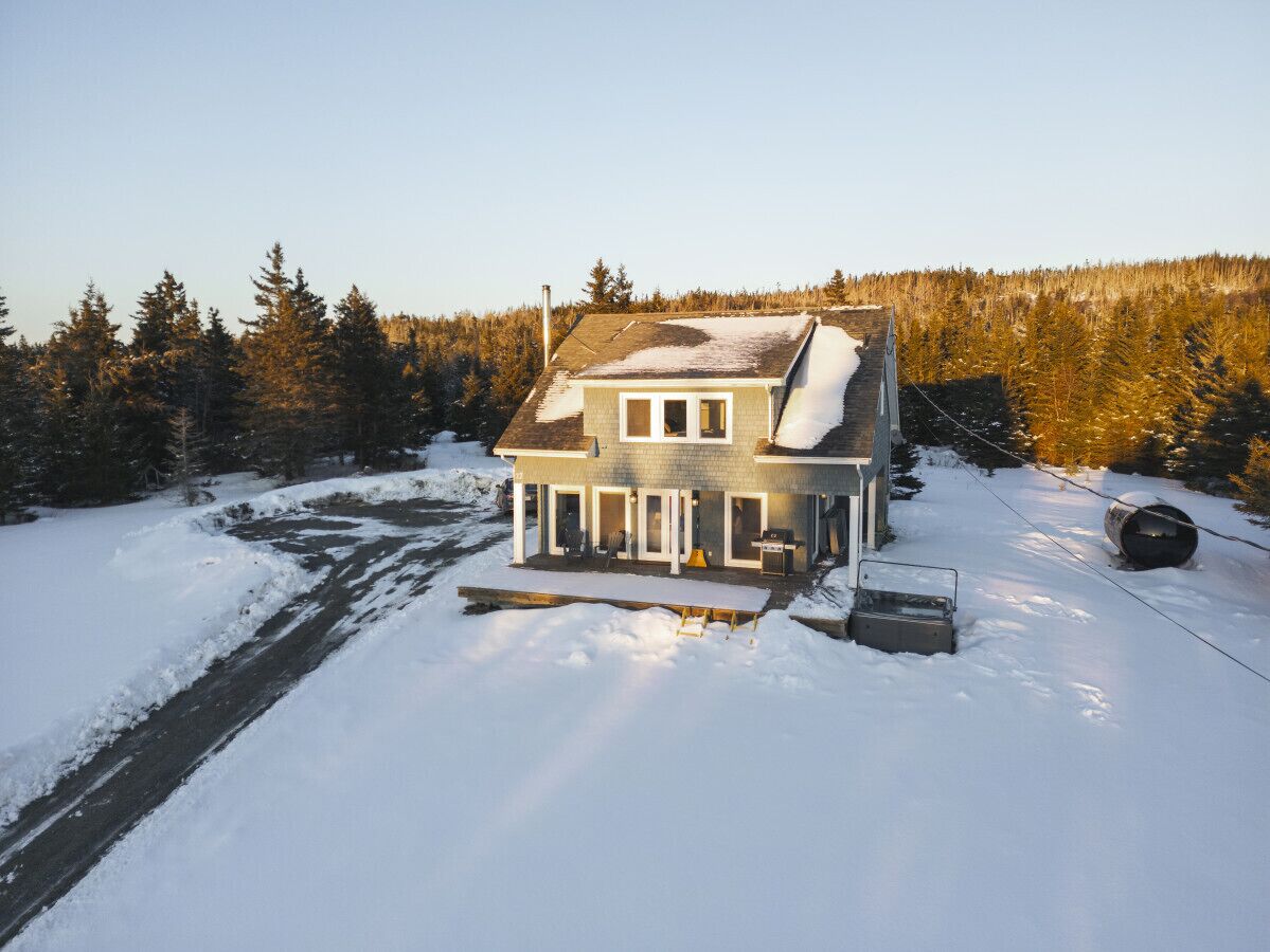 Una casa de dos pisos con un techo cubierto de nieve y un muelle que se adentra en un río.