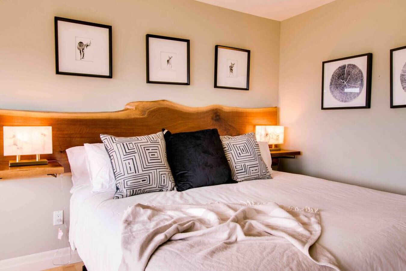 A neatly made bed with patterned pillows, a wooden headboard, and framed pictures on the wall.