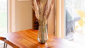 Ein Essbereich mit einem Holztisch, einer Glasvase mit Trockenpflanzen und einer Kronleuchter mit mehreren kugelförmigen Lampen.