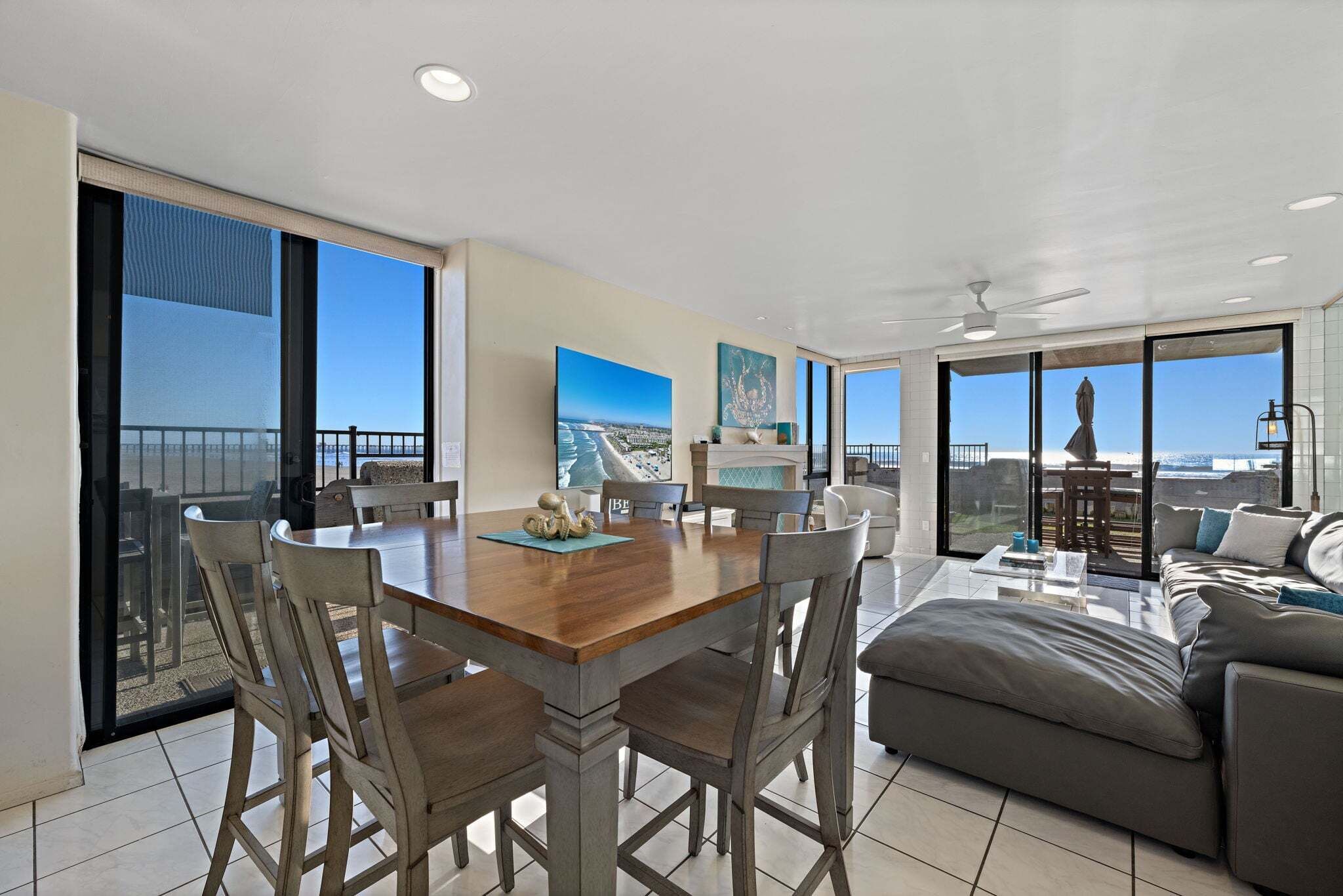 A spacious living area with a dining table, chairs, a sofa, and a balcony with a view of the beach.