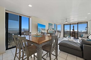 Un vaste espace de vie comprenant une table à manger, des chaises, un canapé et un balcon avec vue sur la plage.