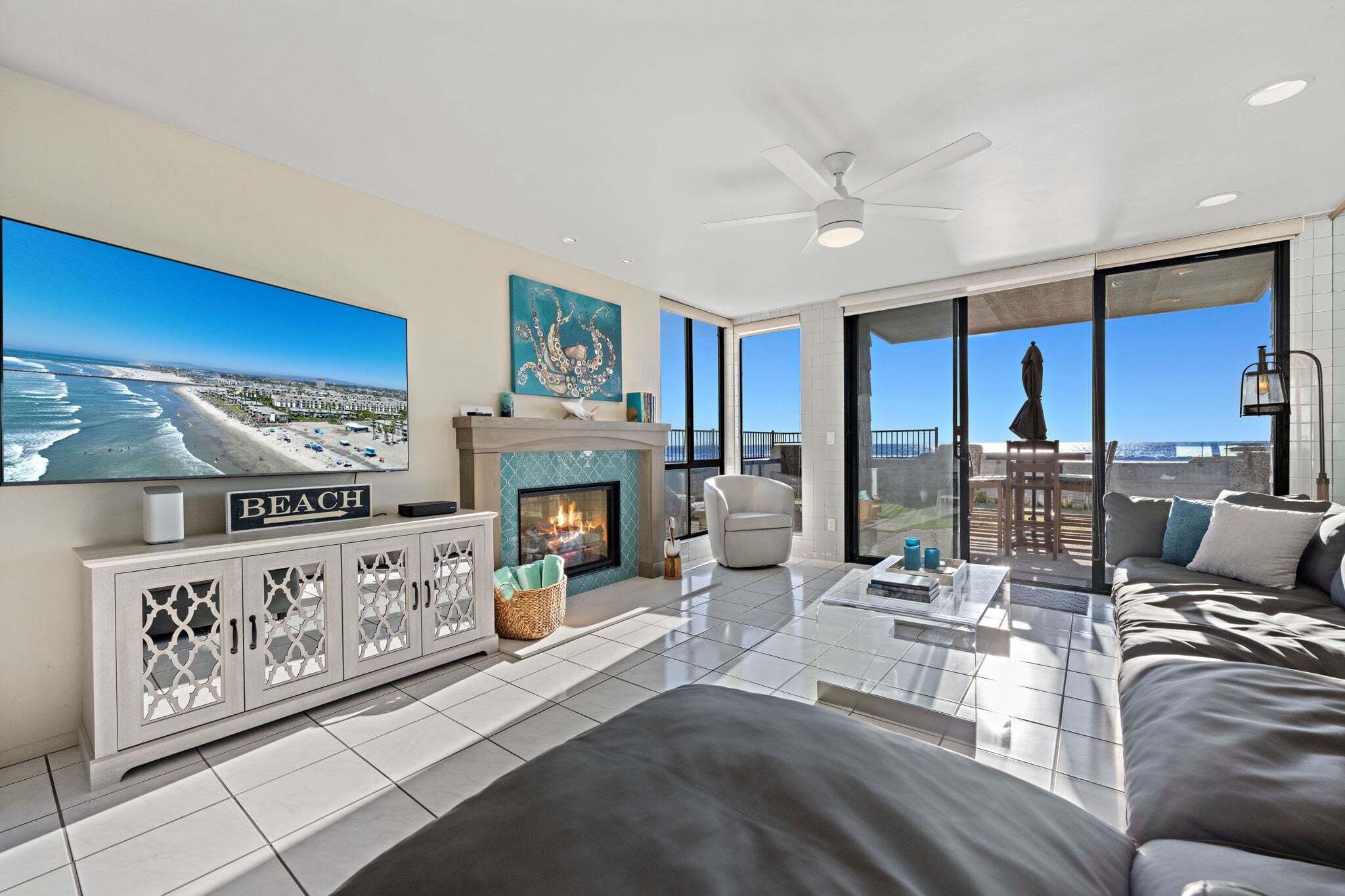 Una sala moderna con chimenea, televisor y ventana grande con vista a la playa.