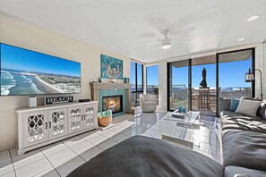 Een moderne woonkamer met een open haard, een televisie en een groot raam met uitzicht op het strand.