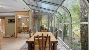 Une véranda équipée d’une table et de chaises, de grandes fenêtres et offrant une vue sur l’extérieur.
