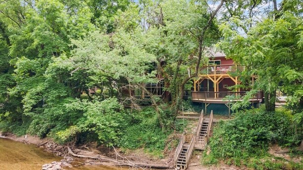 Une maison entourée d’une forêt dense, avec un escalier en bois menant à une terrasse.